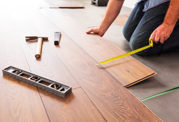 A man laying laminate floor with tape measure