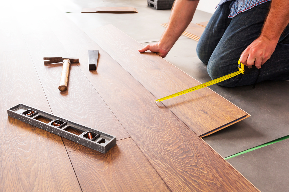 A man laying laminate floor with tape measure